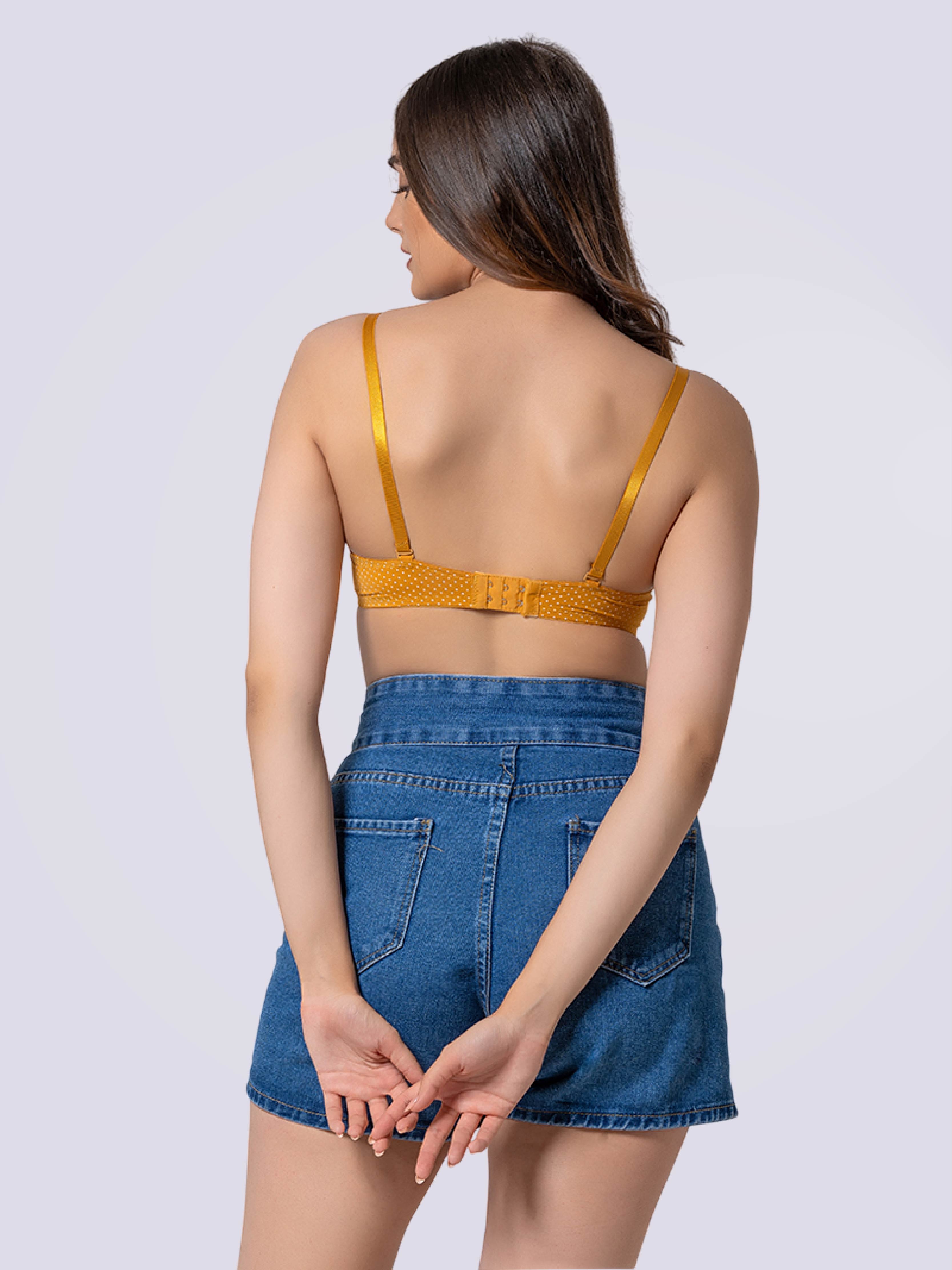 Woman wearing a mustard yellow bralette and blue denim shorts on a white background