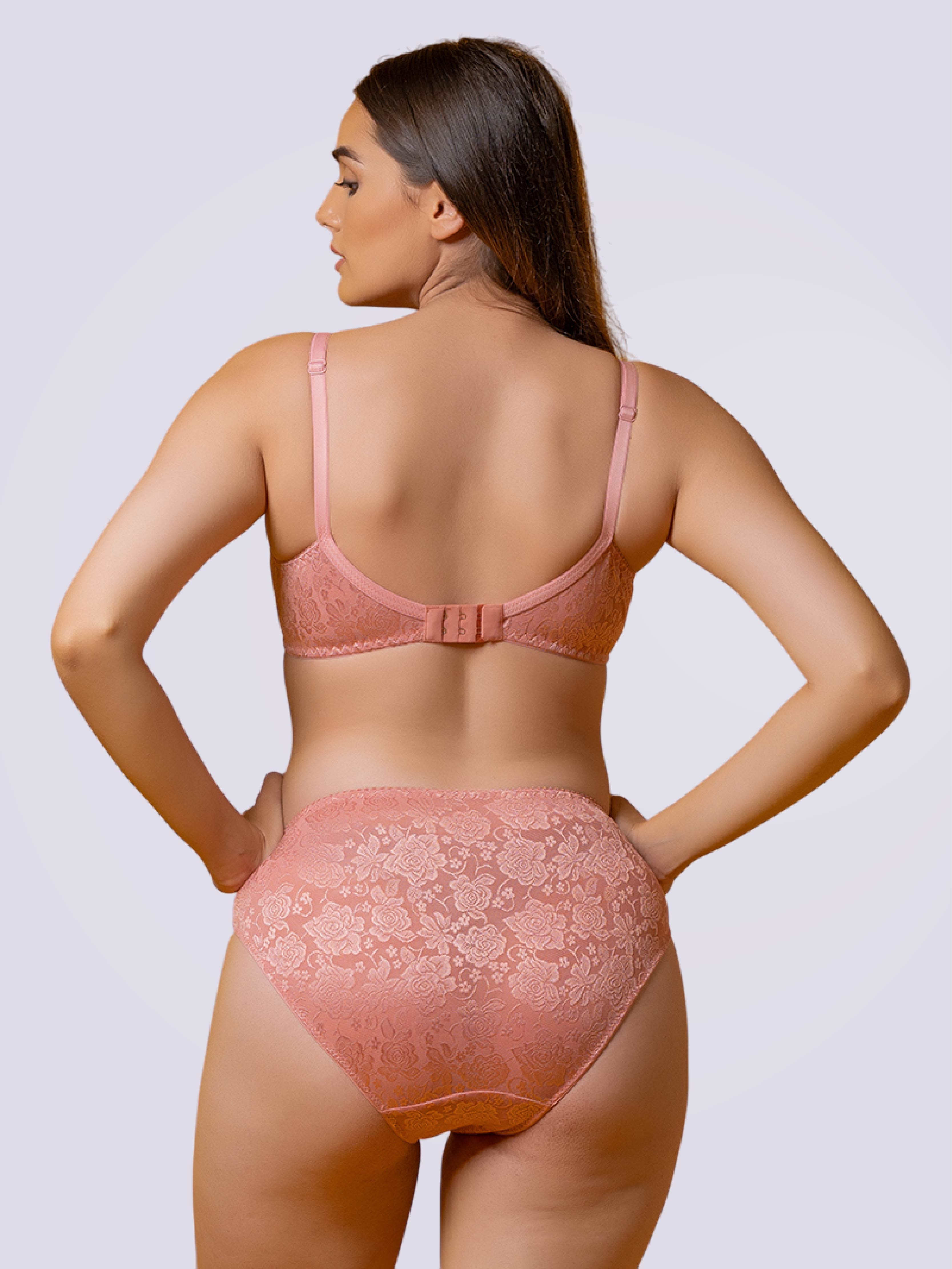 Woman wearing a baby pink lace lingerie set on a plain background