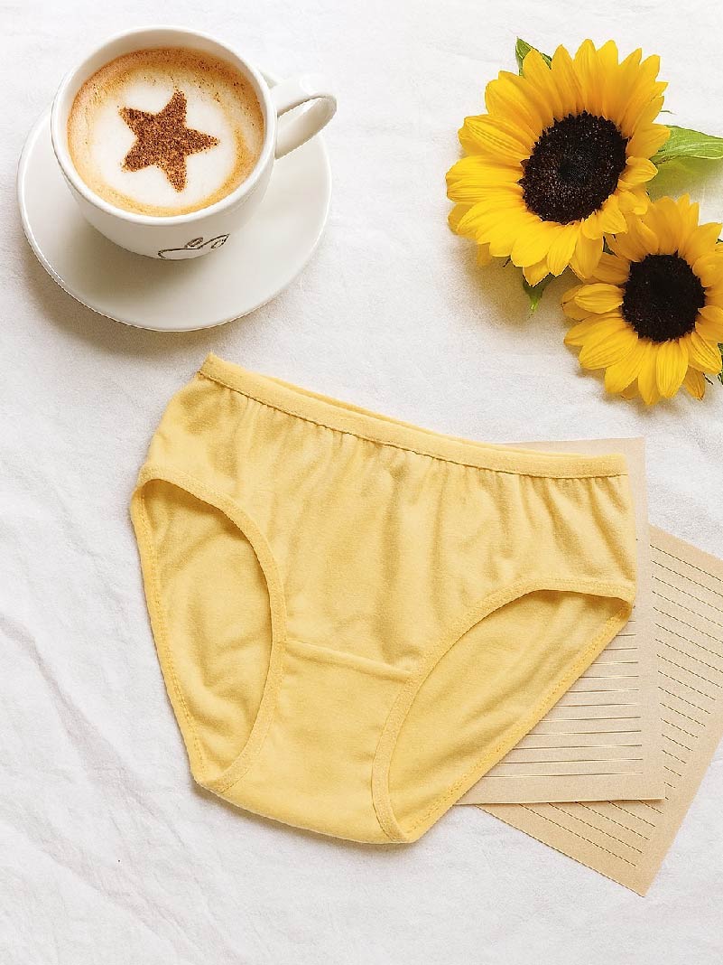 Yellow underwear on a white surface with a cup of coffee and sunflowers.