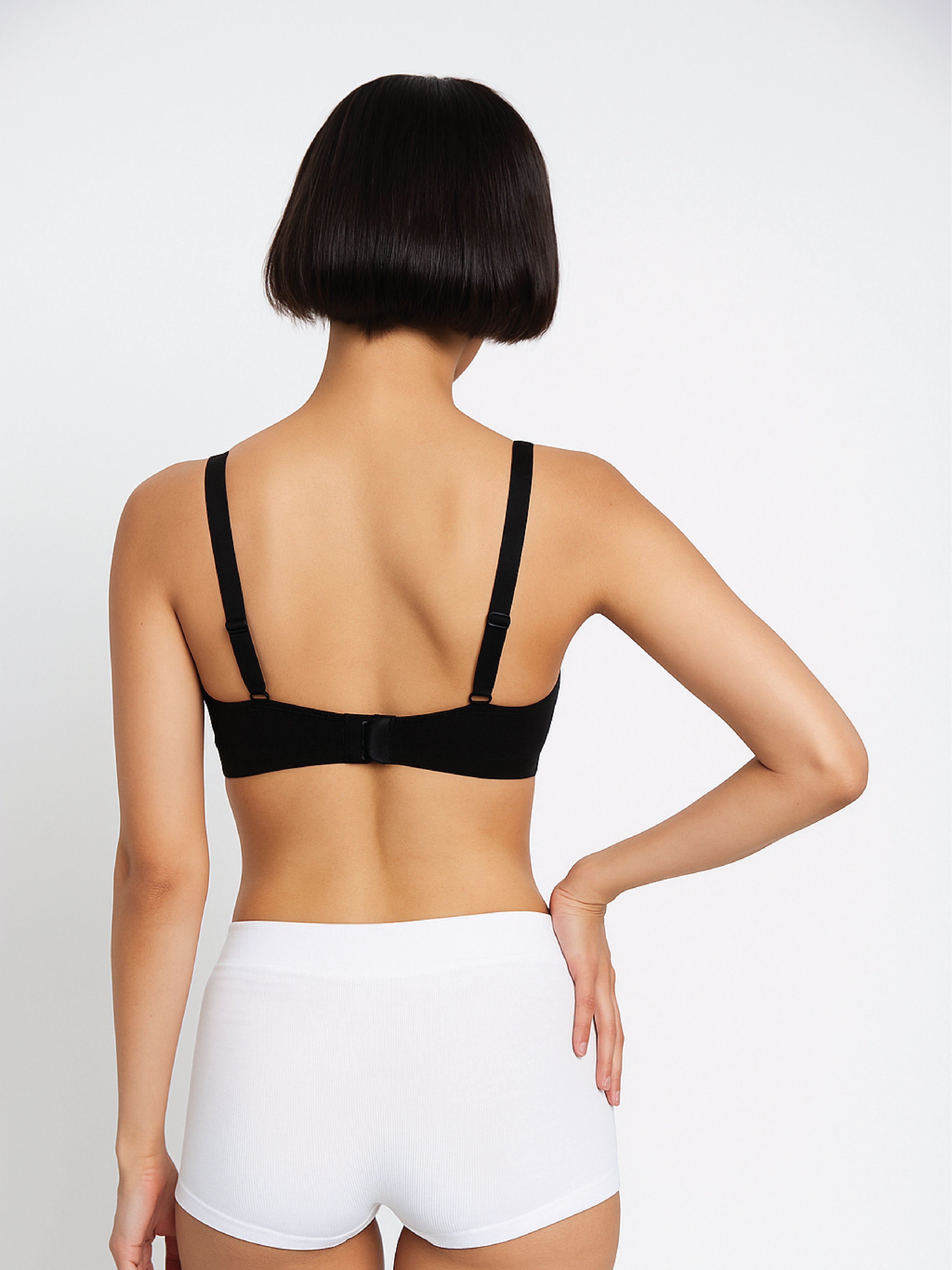 Person wearing a black bra and white underwear on a plain background