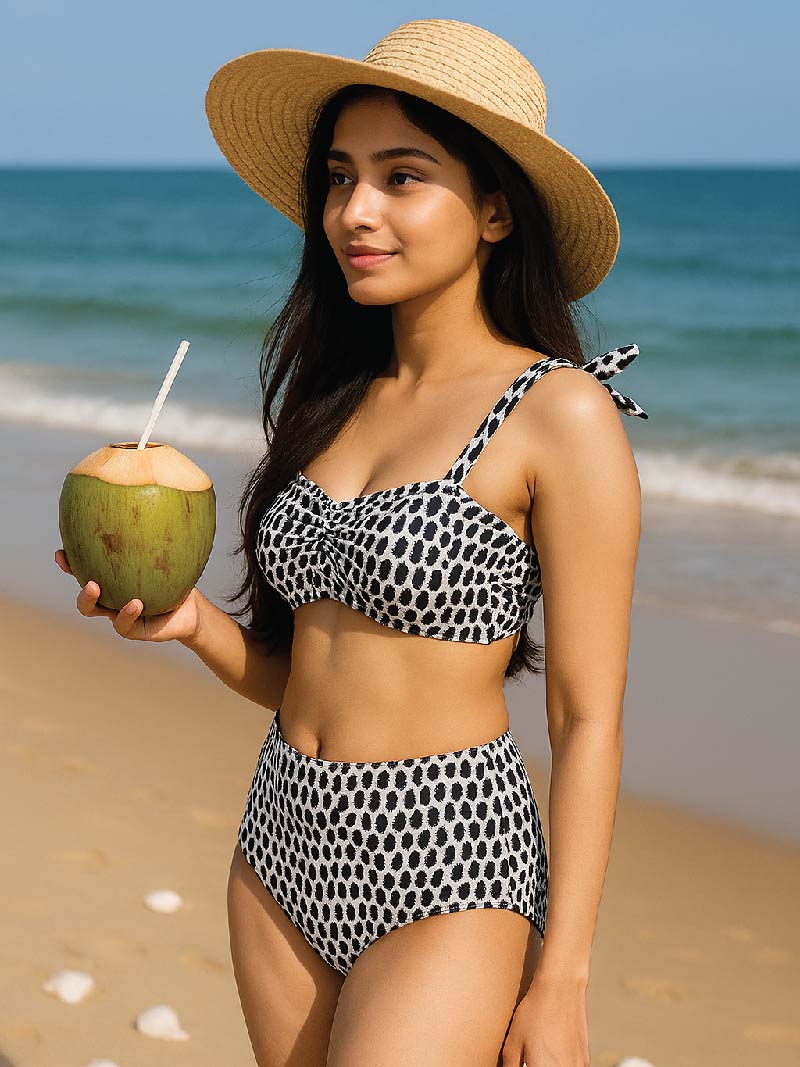 Woman in a polka dot bikini holding a coconut on a beach